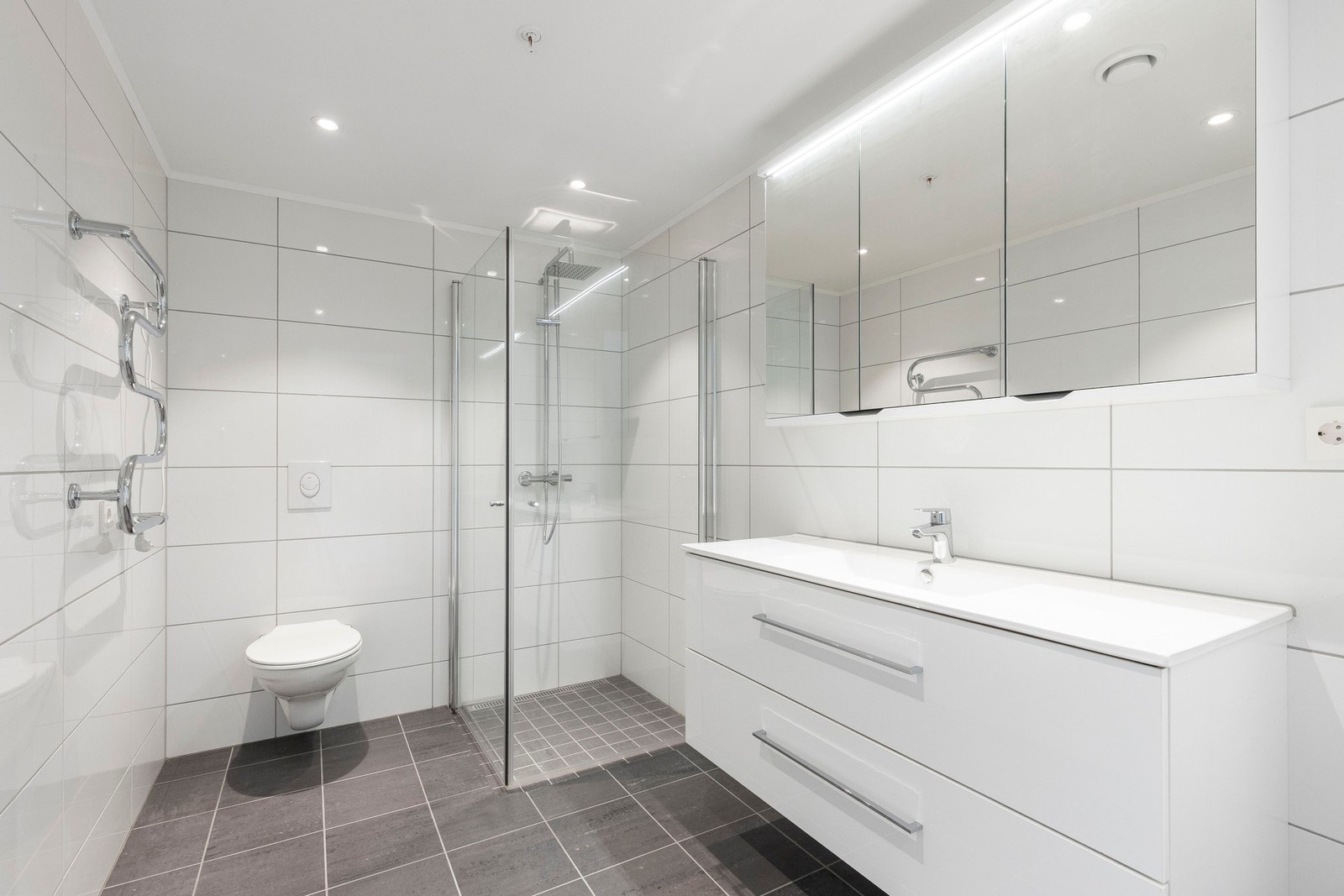 Badet er innredet med dusjnisje med innfellbare glassvegger, toalett og baderomsinnrending med servant. Galleribilde