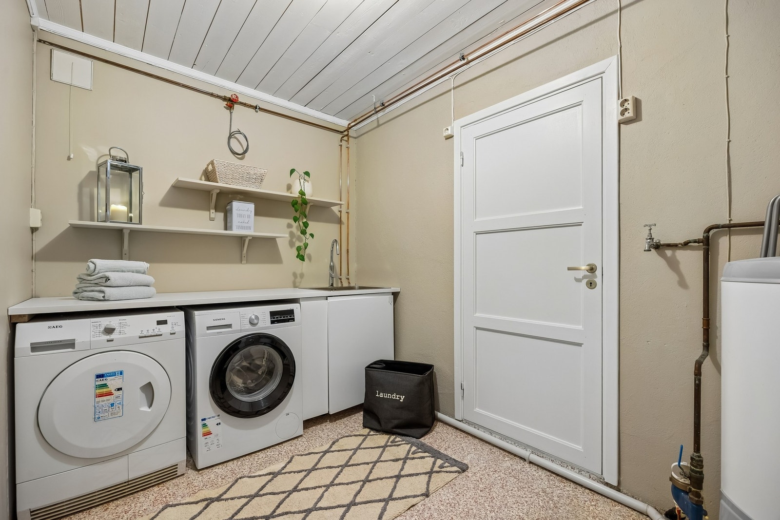 Praktisk vaskerom med benk, oppbevaringshyller, utslagsvask og plass til vaskemaskin og tørketrommel. Galleribilde