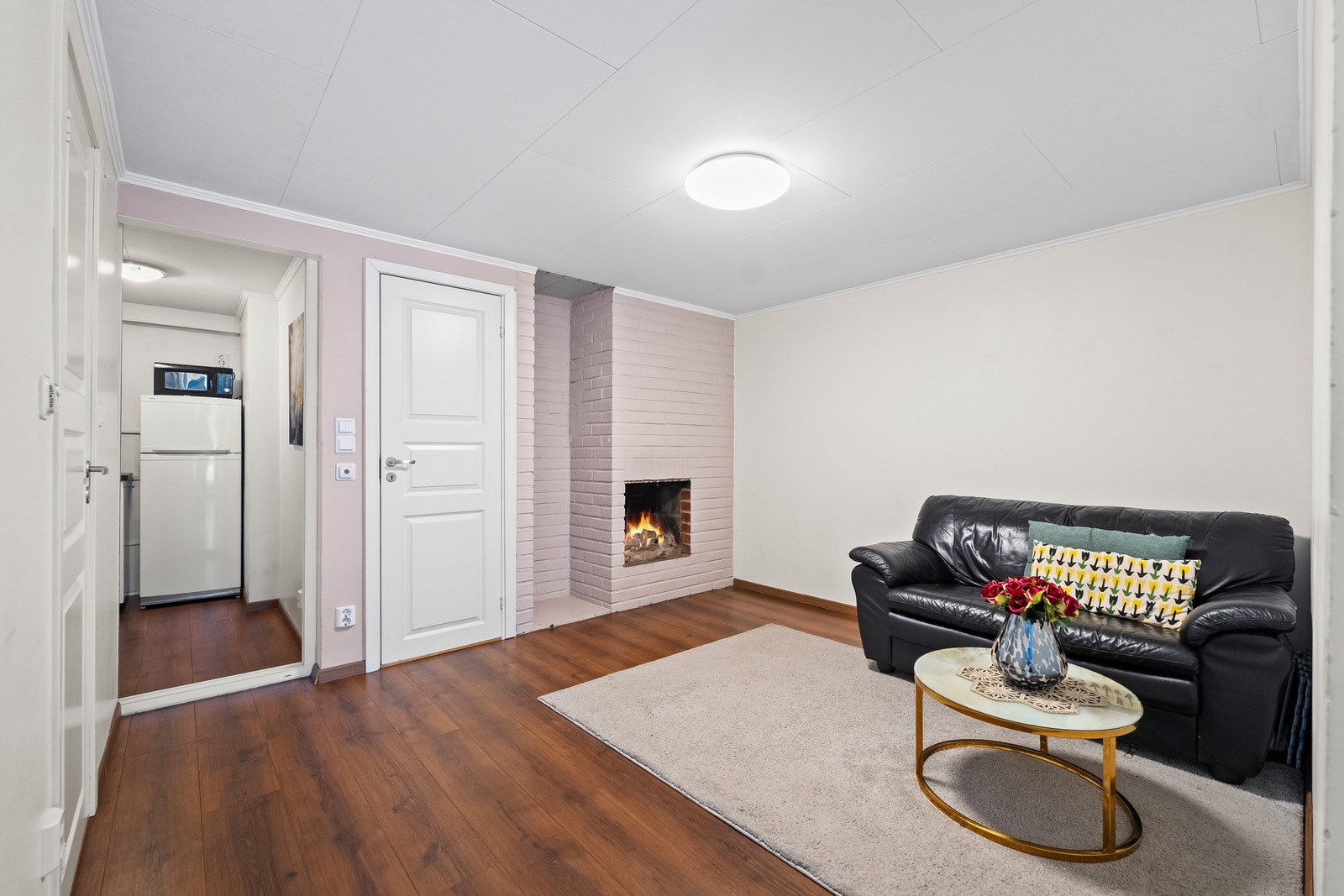 Hybel: Tiltalende stue/oppholdsrom med lysmalte veggflater og laminat på gulv. Det er etablert en åpen peis midt i rommet, men denne er ikke funksjonstestet (usikker tilstand). Galleribilde