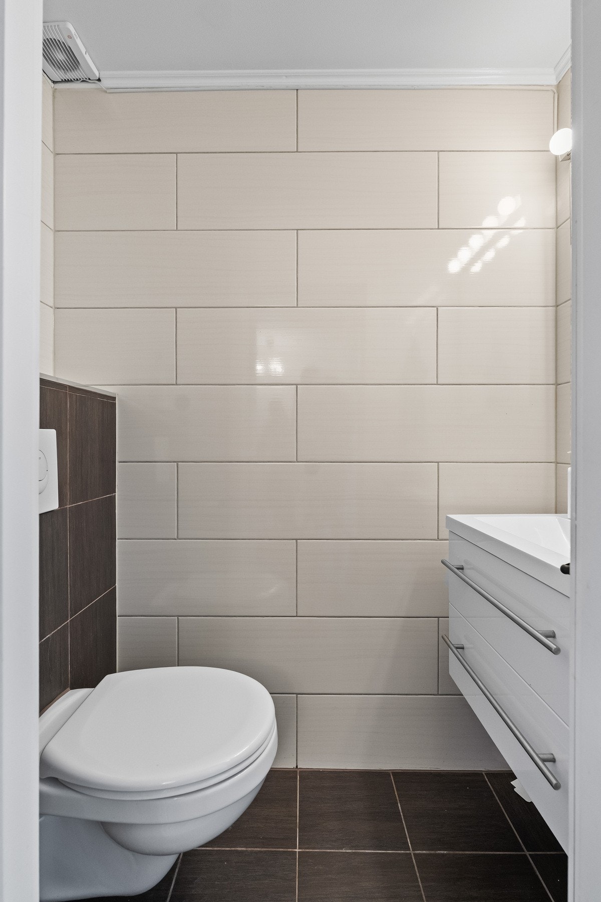 Separat toalettrom vegg-i-vegg med badet, med flislagte overflater, servantmøbel og vegghengt toalett. Galleribilde