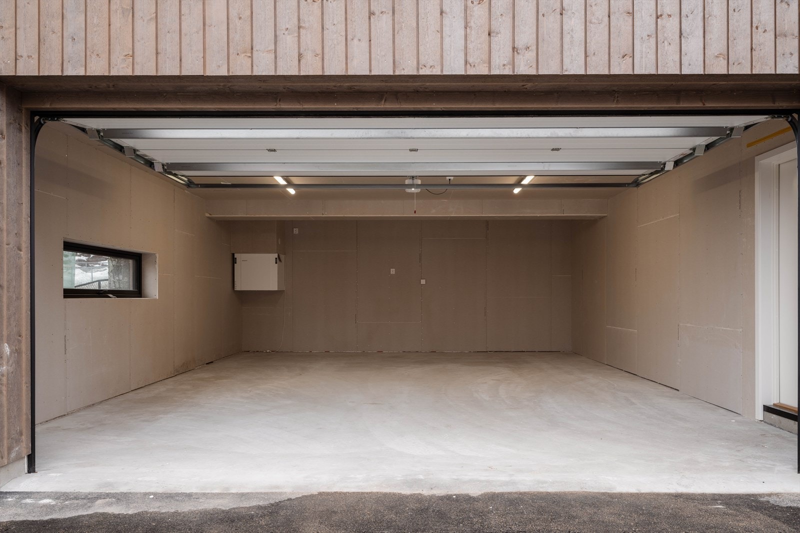 Garasjen leveres med OSB-plater på vegger og tak, samt garasjeport i dempet sort (NCS 8500). Herfra er det dør rett inn til boligen. Galleribilde