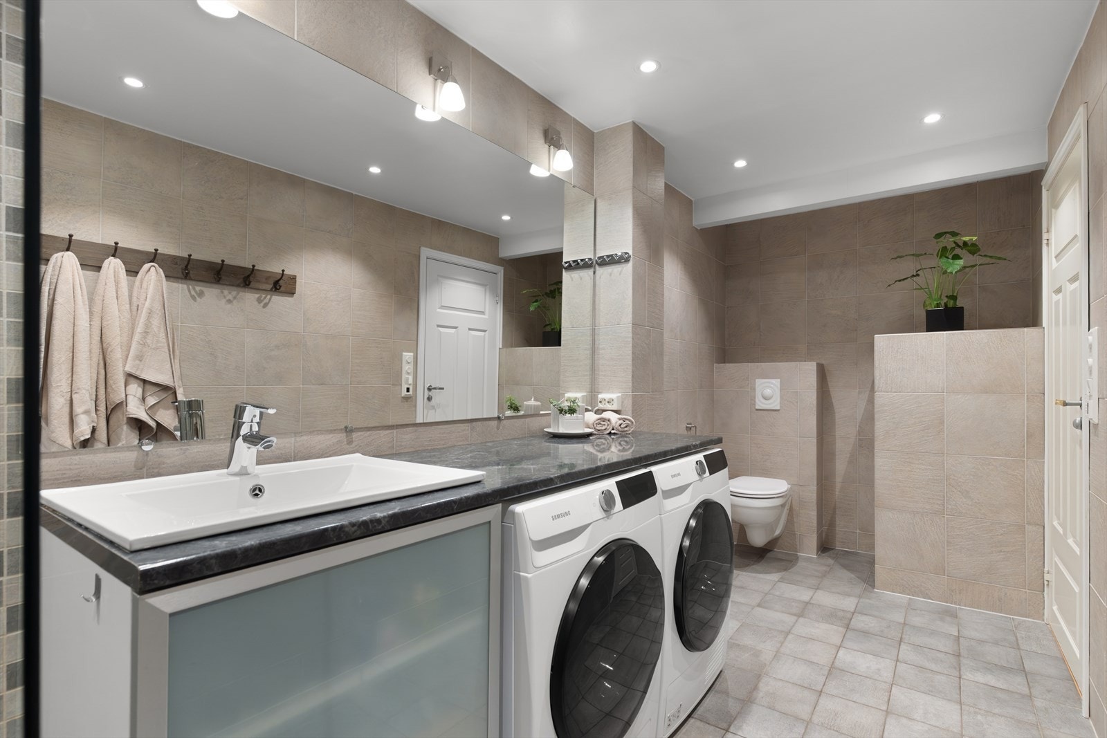 Baderommet har en praktisk servantbenk og plass til vaskemaskin og tørketrommel. Varmekablene styres av Elko Super termostat med Zigbee-tilkobling med mulighet for tilkobling til kompatibelt smarthussystem. Galleribilde