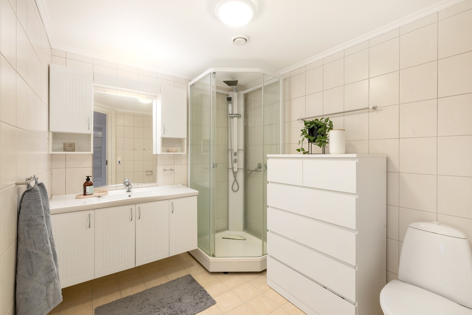 Flislagt bad med varme i gulv. Badet har dusjkabinett, servant med underskap og toalett. Galleribilde