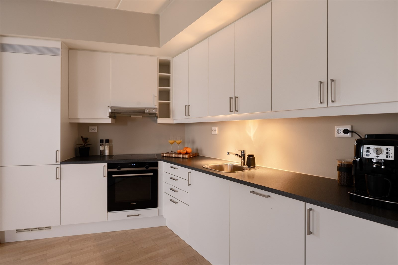Tidløs kjøkkeninnredning fra Sigdal med glatte, fabrikklakkerte fronter og laminat benkeplate. Det er praktisk belysning under overskap som gir godt arbeidslys. Galleribilde