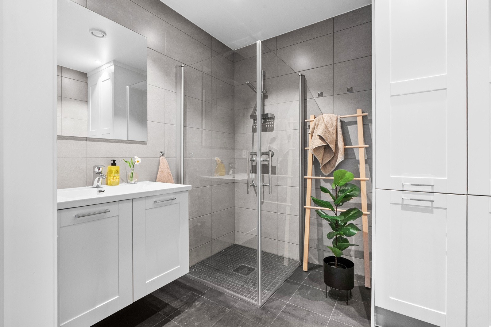 Lekkert, flislagt baderom. Det er innredet med vegghengt servantskap, vegghengt toalett med innebygget sisterne og dusjhjørne med hengslede glassdører. Galleribilde