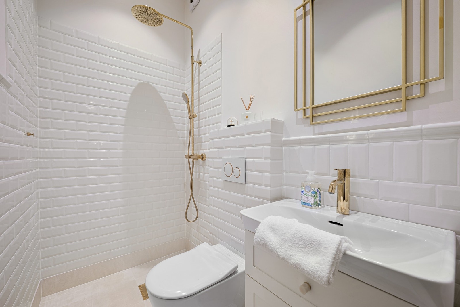 Baderom i gangen. Baderomsinnredning med glatte, folierte fronter. Speil med lys på vegg over servanten. Dusjhjørne med regnfallsdusj. Galleribilde