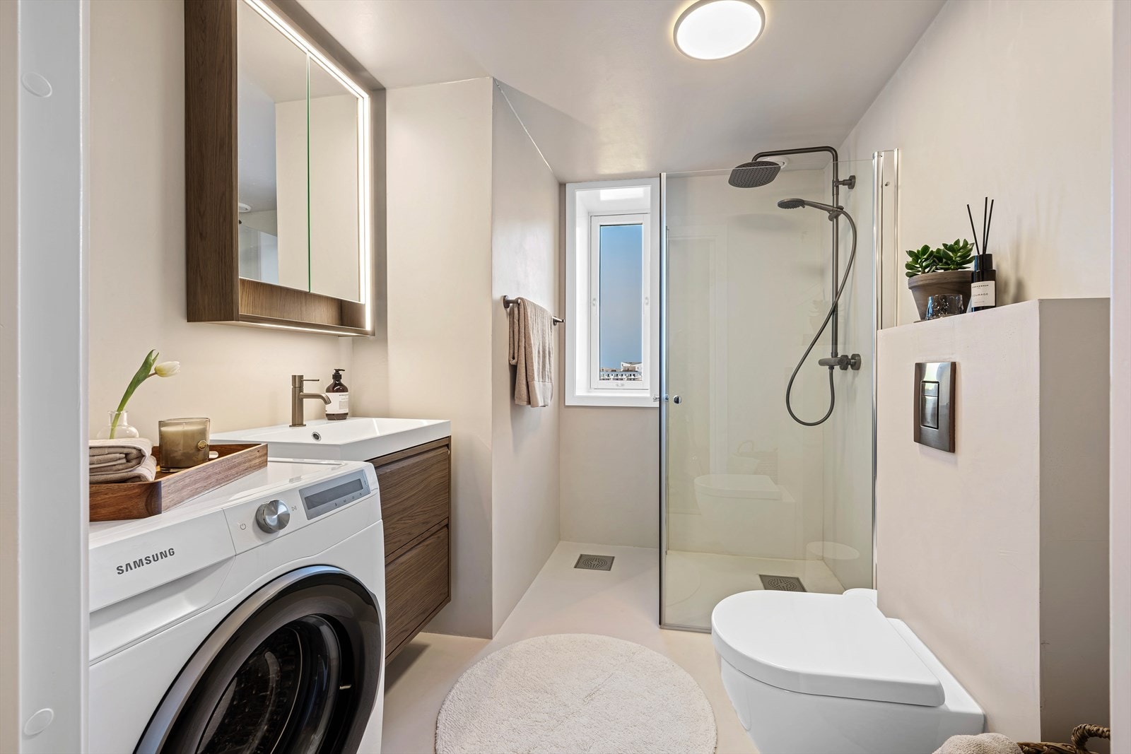 Badet er ellers utstyrt med regndusj, vegghengt toalett og praktisk baderomsinnredning som gir god lagringsplass og speil med LED-belysning. I tillegg har man opplegg for vaskemaskin og plass til tørketrommel. Galleribilde