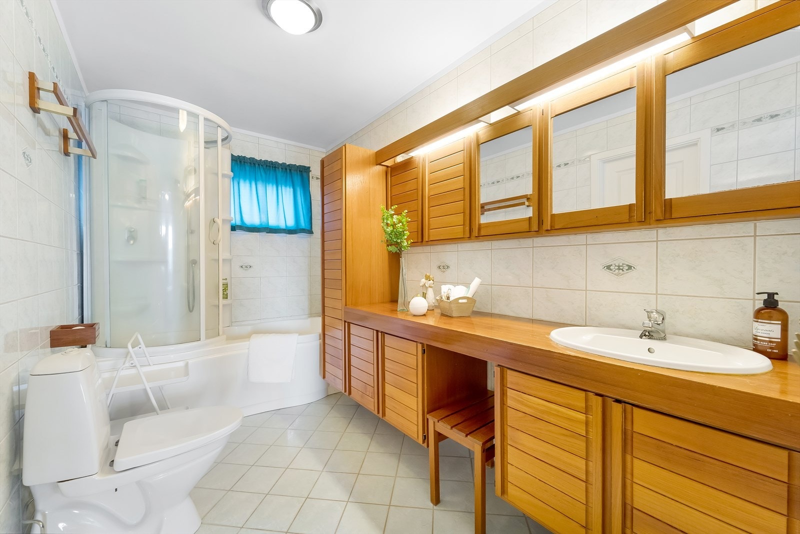 Badet har fliser på gulv og vegger. Badet er innredet med baderomsinnredning, toalett og badekar med dusjløsning. Galleribilde