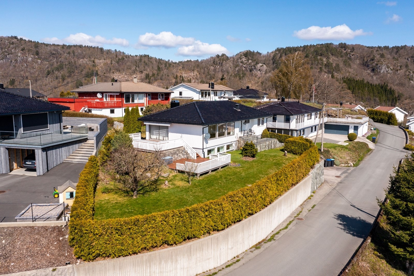 Boligen ligger på en høyde, fint opparbeidet med støpt betongmur, hekk, plen og beplantning. Galleribilde