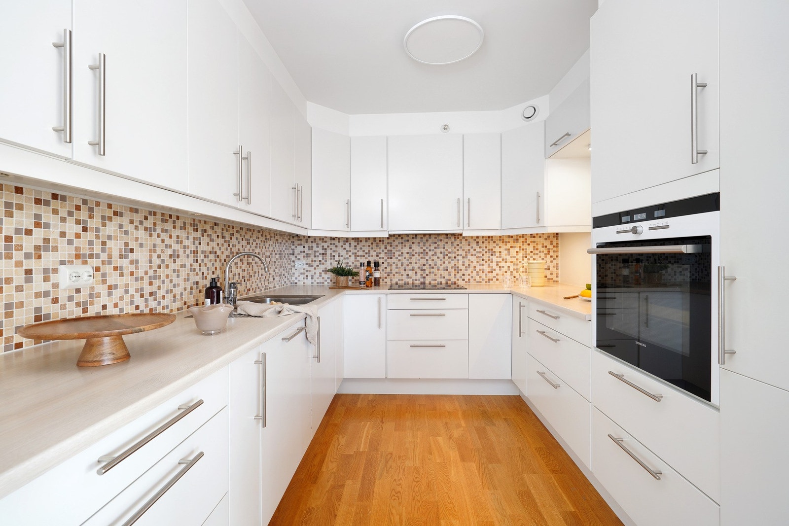 Tidløst kjøkken med hvite fronter, rikelig skap- og benkeplass samt integrerte hvitevarer (stekeovn, kjøleskap og oppvaskmaskin) Galleribilde