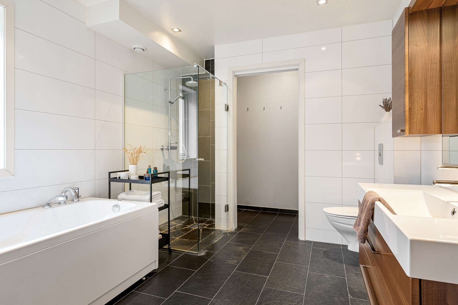 Dusjhjørne med glassvegger, badekar, vask i seksjon, vegghengt wc og speil med belysning. Varmekabler i gulv og spotter i tak. Galleribilde