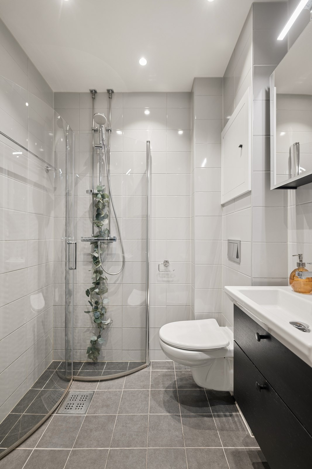 Varmekabler i gulvet sørger for en behagelig temperatur året rundt. Rommet er innredet med et stilren servant med nedfelt vask, veggmontert toalett og dusjhjørne med glassvegger som gir en åpen og romslig følelse. Galleribilde