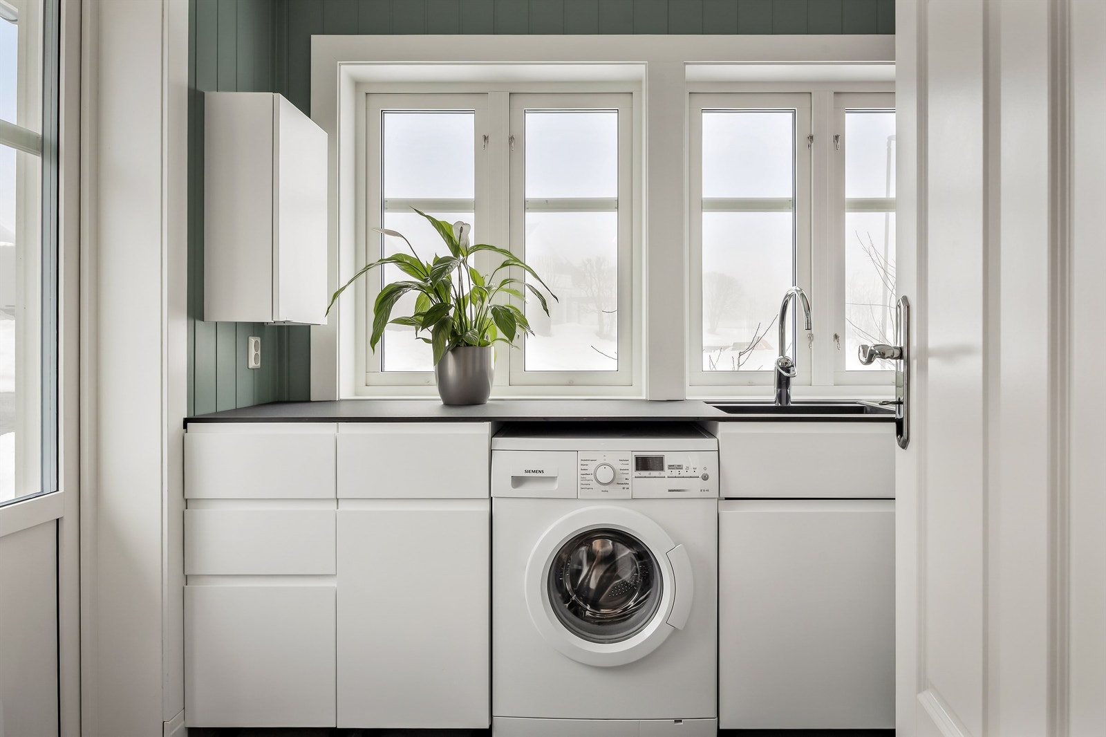 Praktisk vaskerom med egen inngang, skapinnredning, benkeplate i kompositt og opplegg for vaskemaskin. Galleribilde