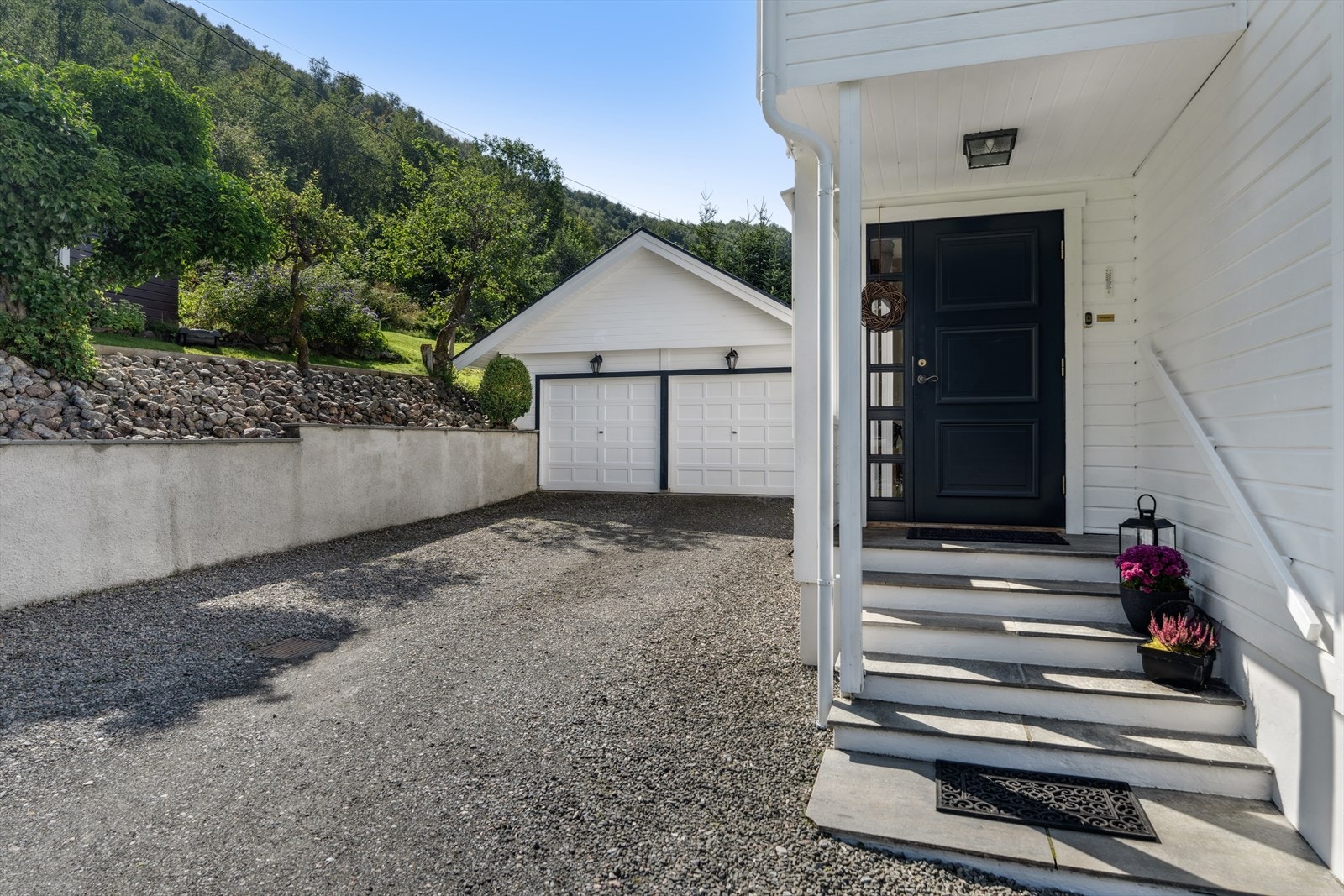 Garasjen fra 1991 har leddporter med elektrisk portåpner og innlagt strøm. Overbygget inngangsparti med trappetrinn i skiferheller. Galleribilde