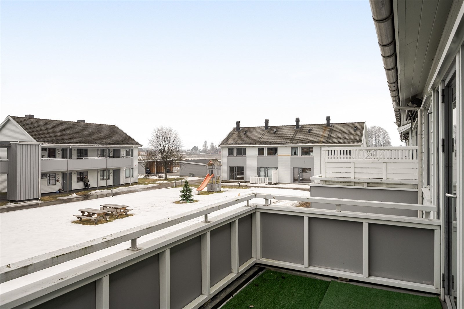 Utsikt fra balkongen mot fellesareal med plen og lekestativer. Galleribilde