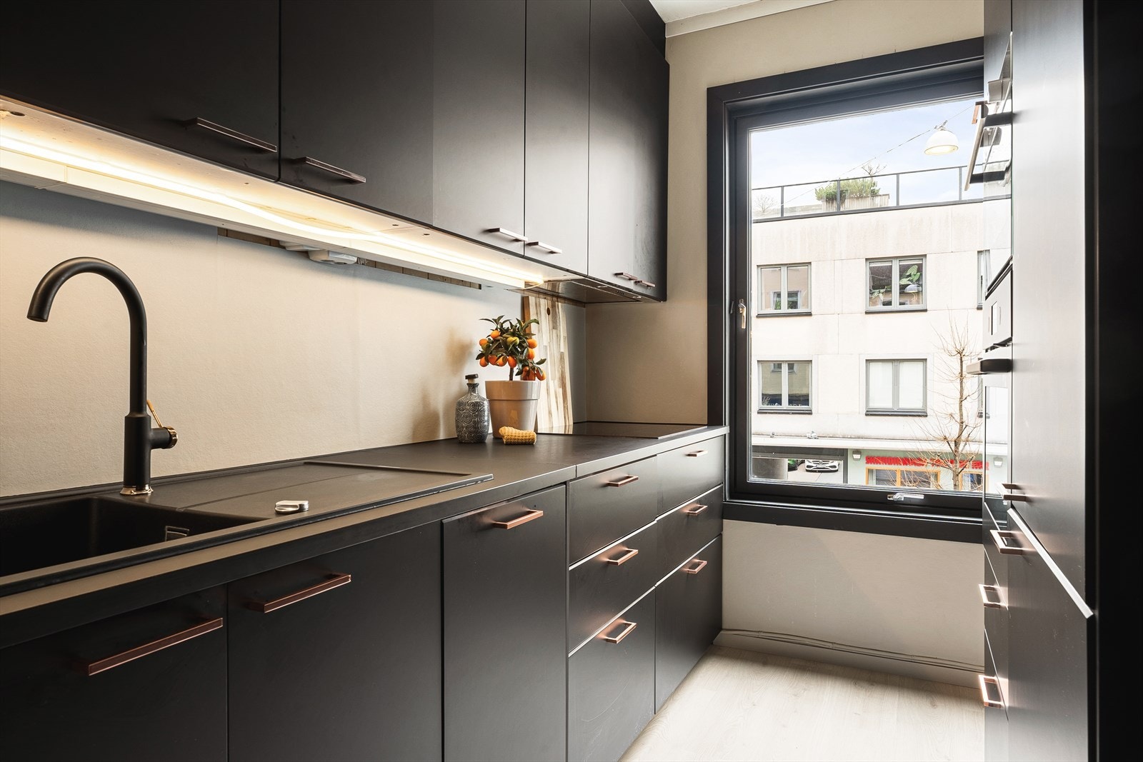 Delikat kjøkkeninnredning med mørke slette fronter, benkeplate i laminat og integrerte hvitevarer. Galleribilde