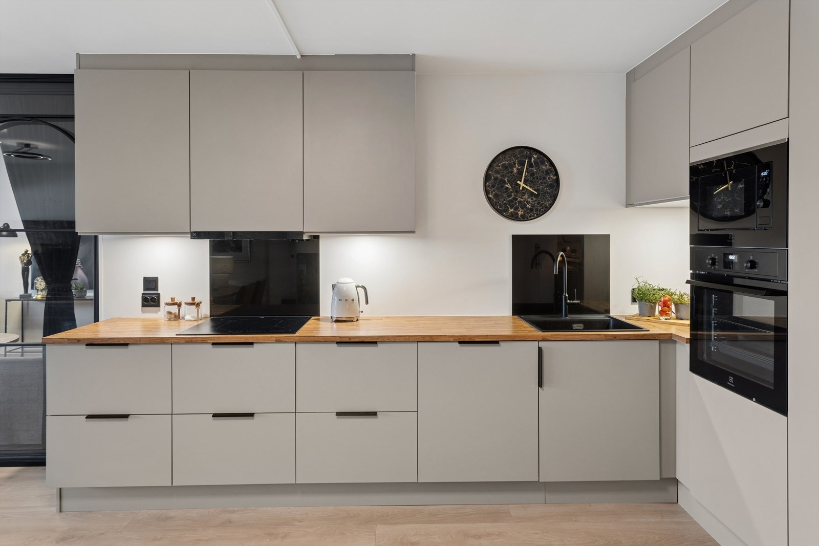 Lyst kjøkken med gjennomført design. Det er platetopp Zephyr, Miele oppvaskmaskin samt kjøkkenvegg beskyttelse med sort glass. Galleribilde