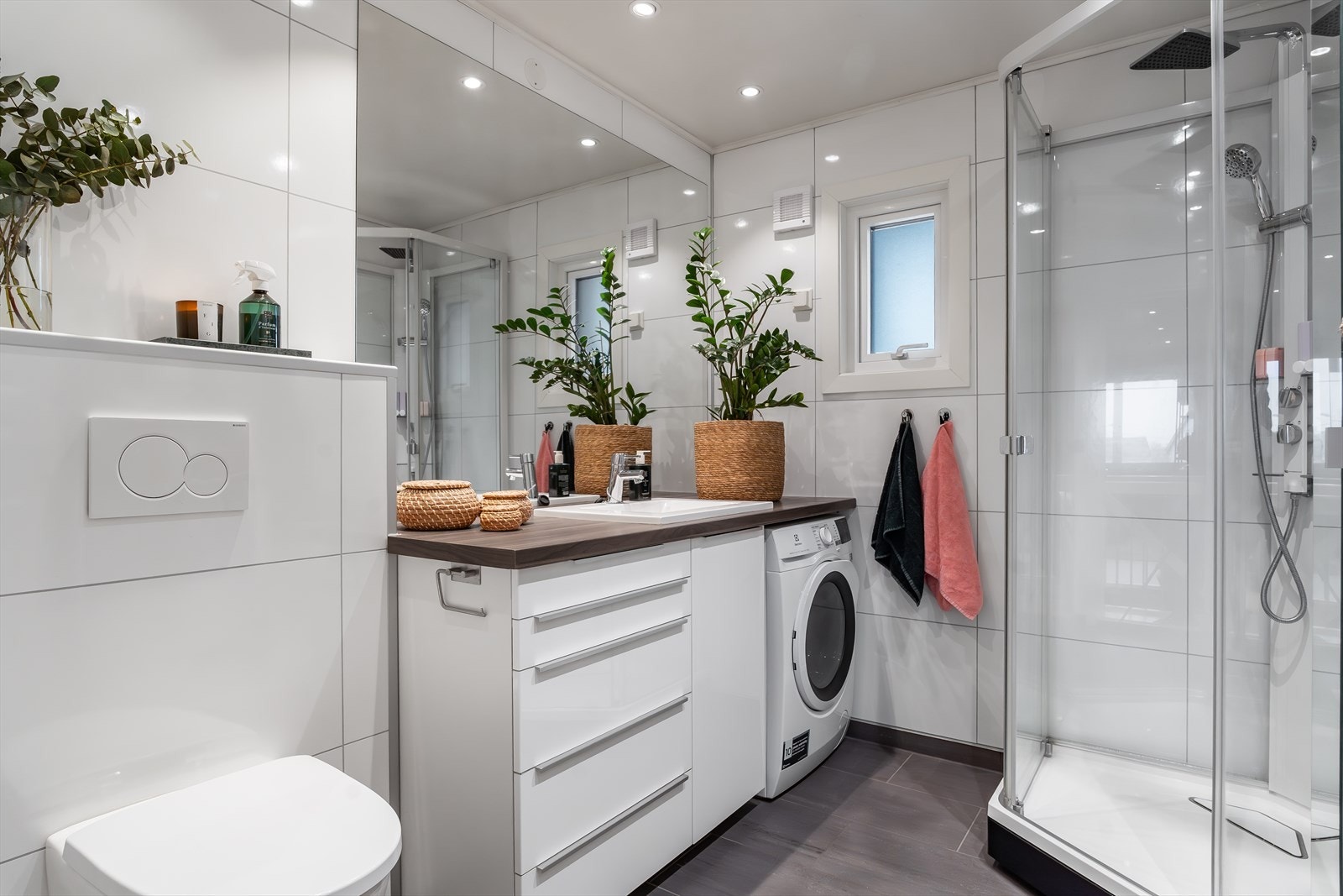 Innbydende baderom med baderomsseksjon, dusjkabinett, vegghengt toalett og opplegg for vaskemaskin Galleribilde