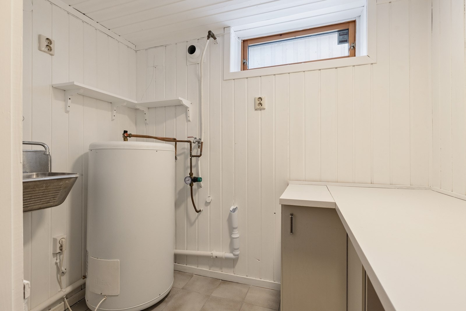 Praktisk vaskerom med opplegg for vaskemaskin, utslagsvask og boligens varmtvannstank. Galleribilde