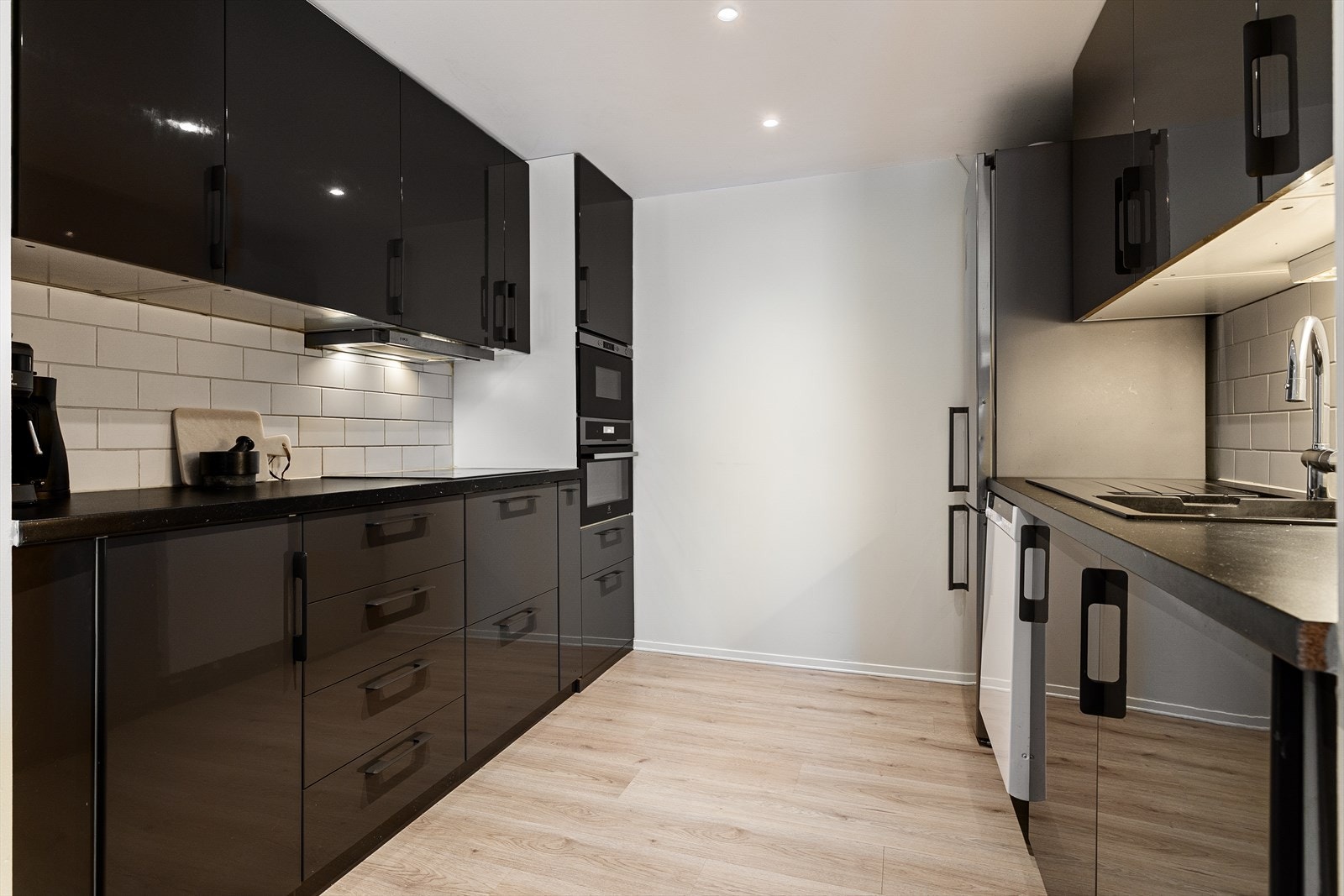 Pent kjøkken med sorte fronter og integrerte hvitevarer som mikro, stekeovn og platetopp. Kombinert kjøl/frys og oppvaskmaskin er frittstående. Galleribilde