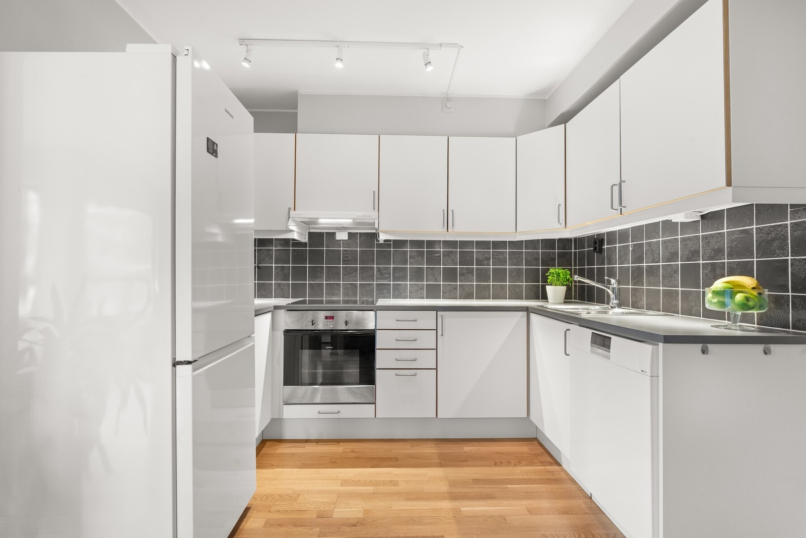 Pent kjøkken i delvis åpen løsning mot stuen, med glatte folierte fronter. Galleribilde