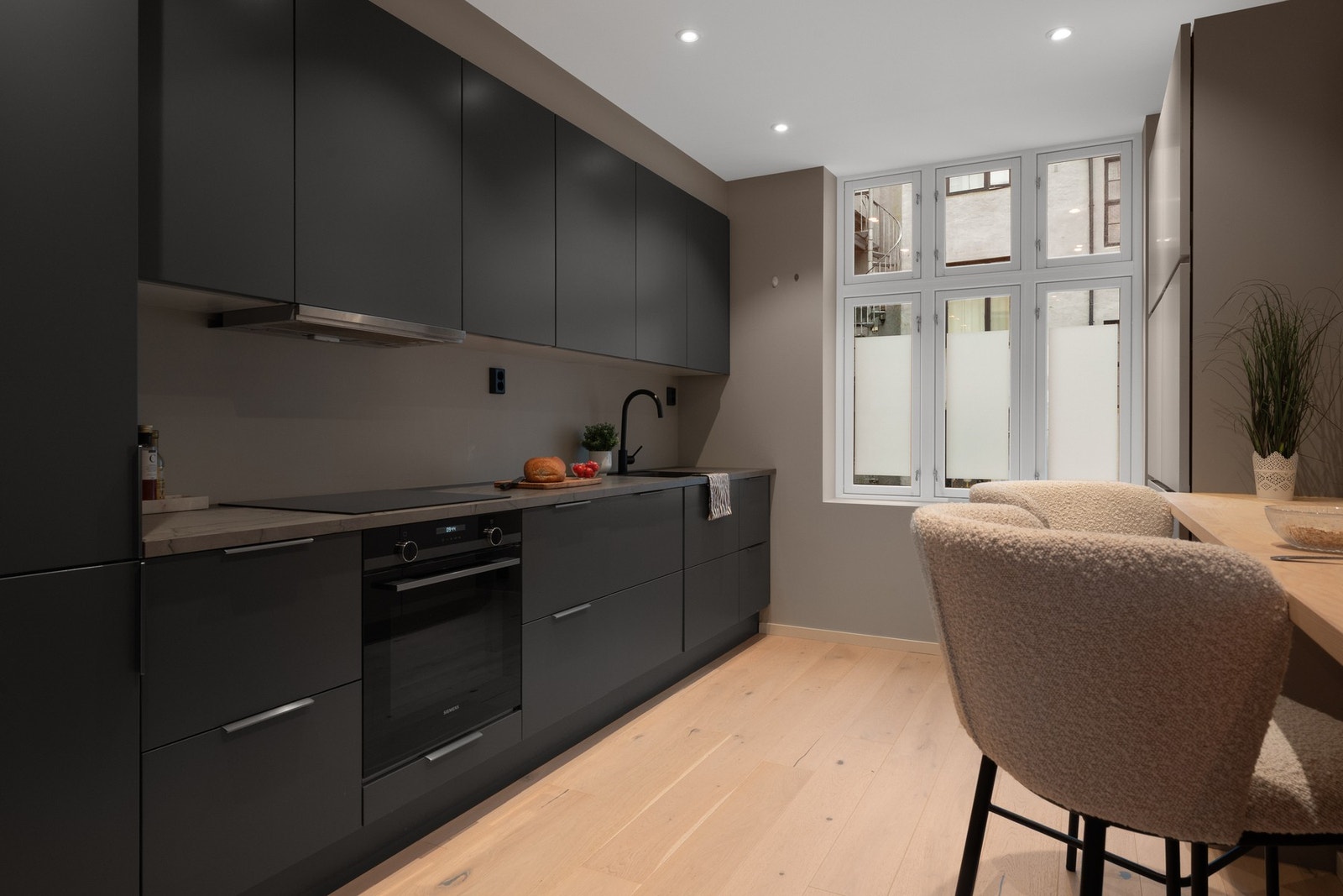 Innredningen har mørke fronter som gir et elegant uttrykk, kombinert med lys benkeplate og integrerte hvitevarer. Galleribilde