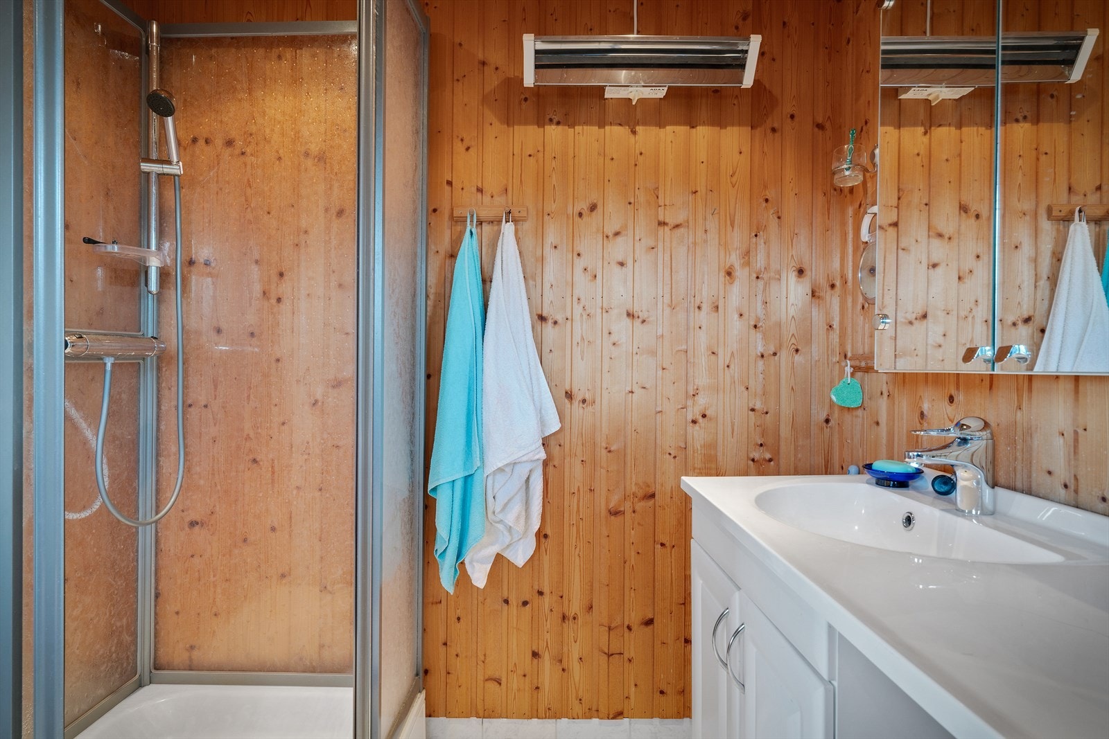 Badet har dusjkabinett, toalett og panel på veggene. Galleribilde