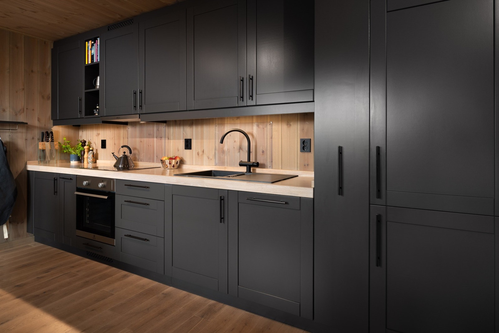 Innredning med profilerte behandlet fronter, solid heltre benkeplate og integrerte hvitevarer. Splashguard på vegg ved platetopp og vask. Galleribilde