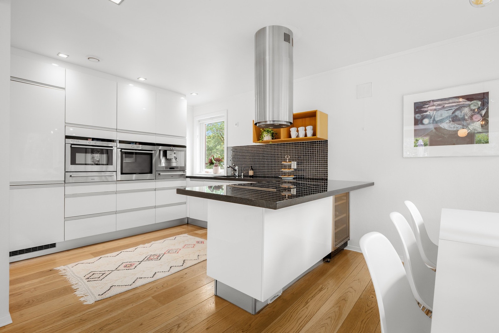 Kjøkkenhalvøyen med nedfelt platetopp, vinskap og ekstra skapplass gir både gode arbeidsflater og en sosial løsning mot spiseplassen. Galleribilde