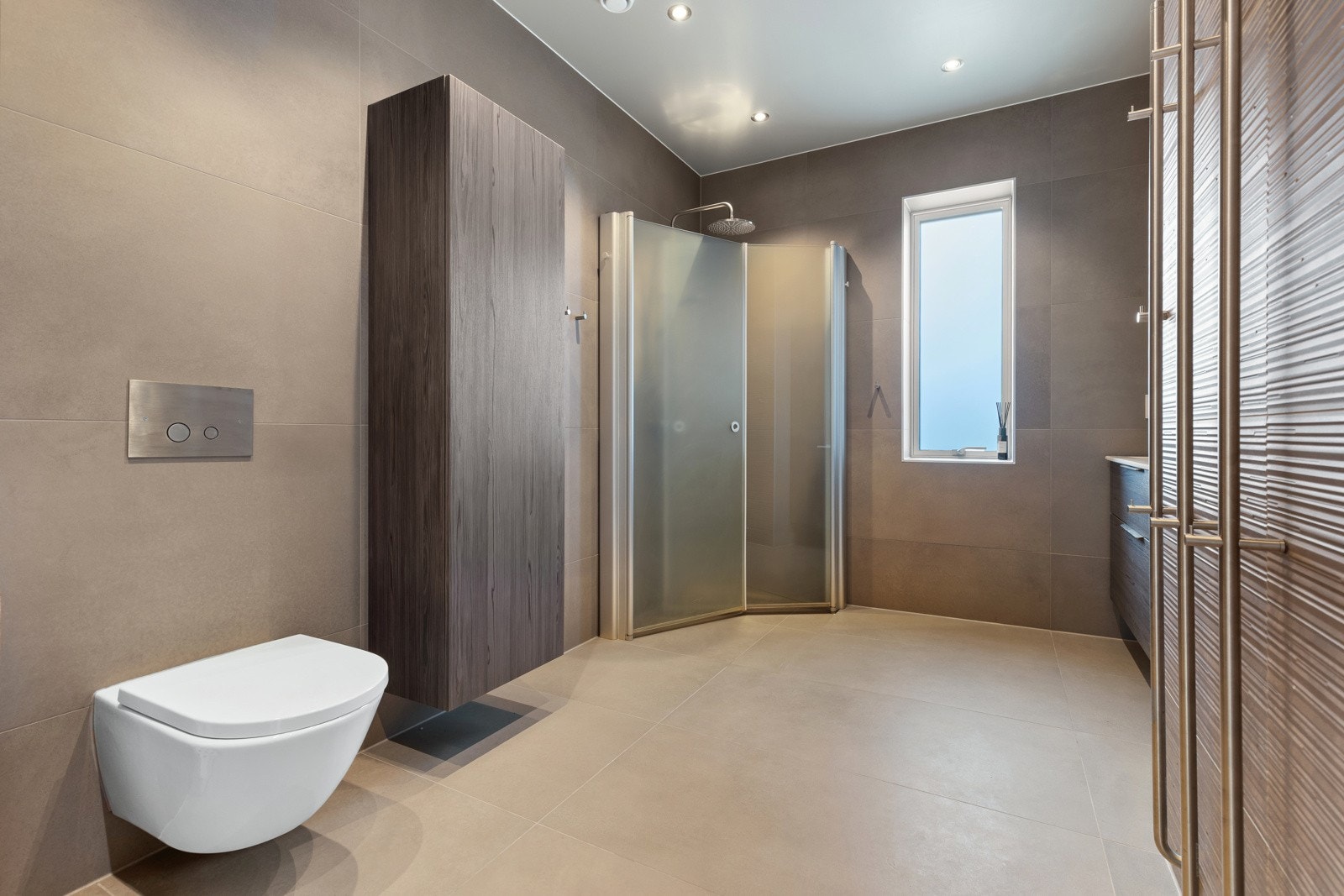 Separat dusjhjørne med innfellbare glassdører og regnfallsdusj. Himlingen er lyssatt med downlights. Galleribilde