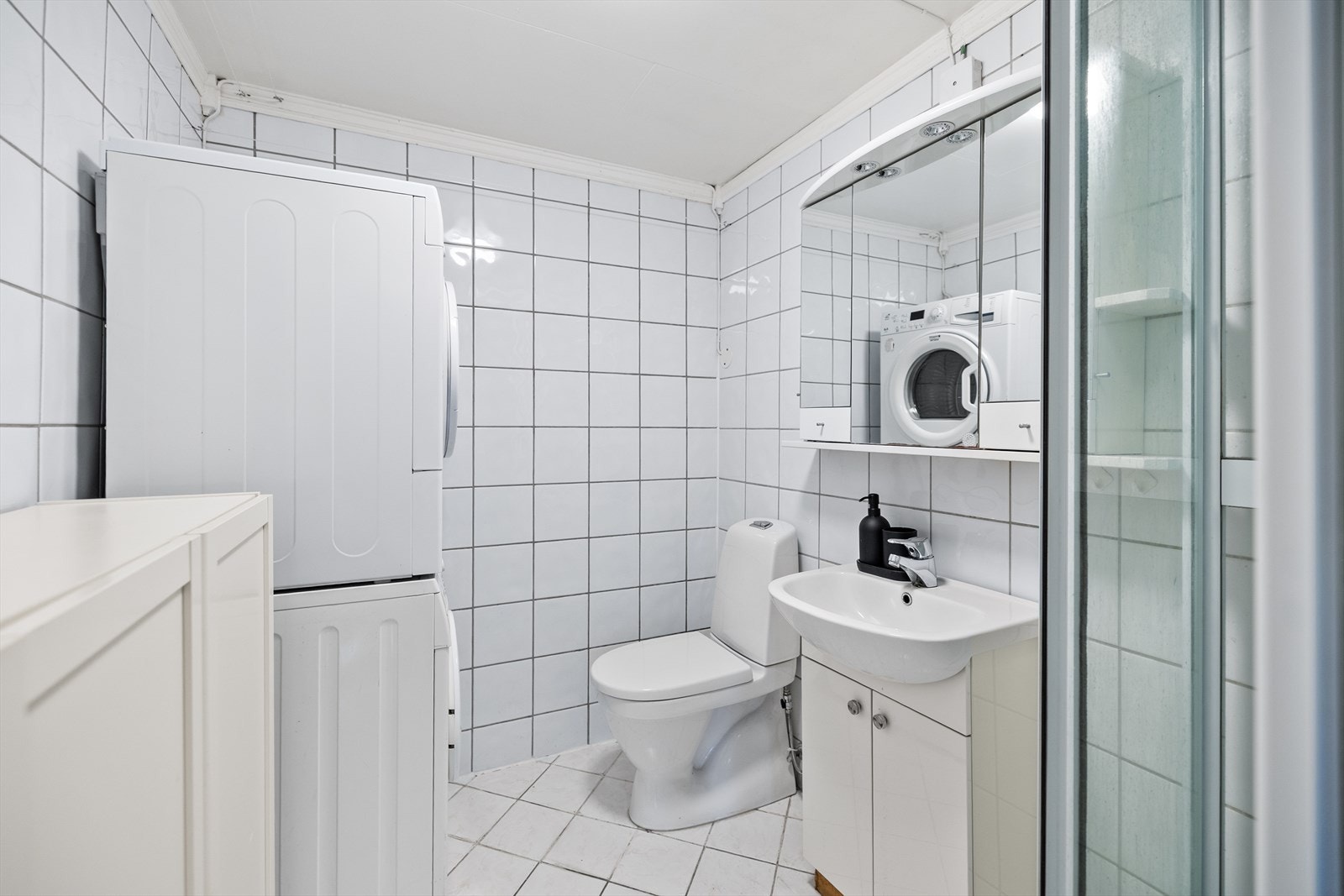 Badet i hybel inneholder innredning med servant, speilskap, gulvmontert toalett (2023), dusjkabinett, samt opplegg til vaskemaskin og tørketrommel. Galleribilde