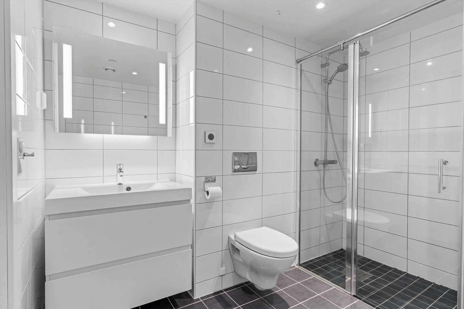 Badet er utstyrt med vegghengt toalett, dusjhjørne med innfellbare glassdører og opplegg for vaskemaskin. Galleribilde