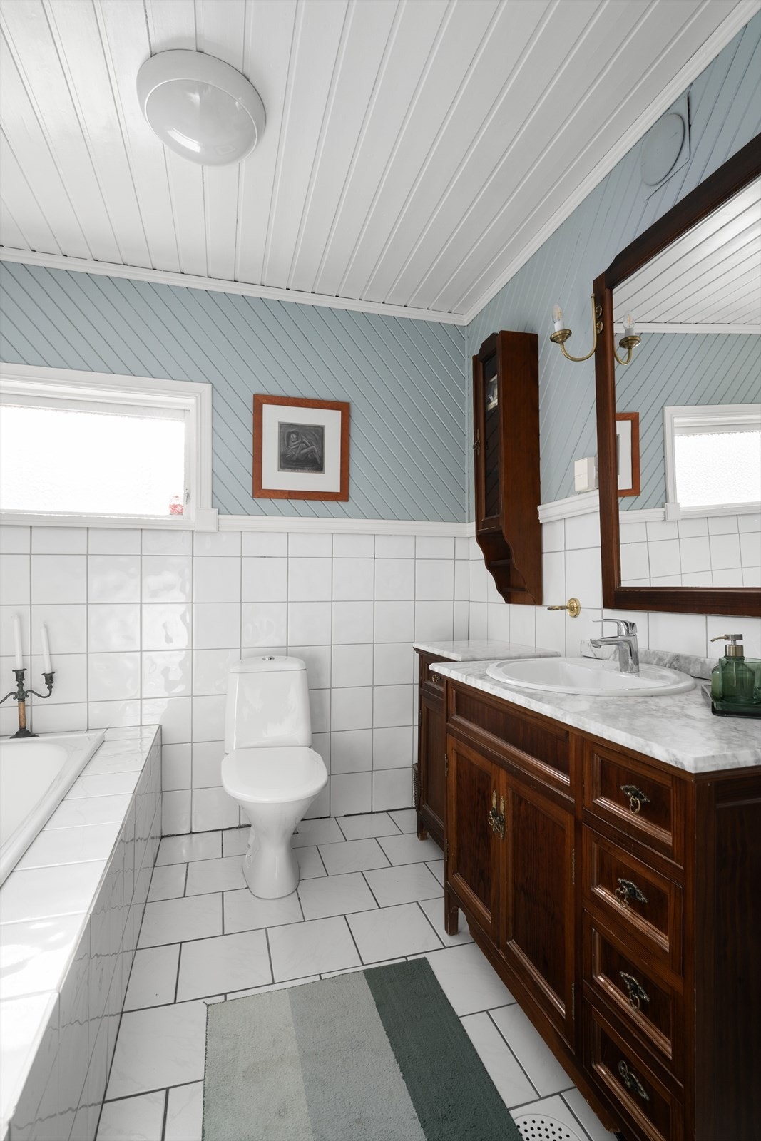 Badet fra midten av 1980-tallet har flislagt gulv med varmekabler, hvor fliser er videreført delvis opp på veggen. Her er det innredning i mørk utførelse med nedfelt servant. Galleribilde