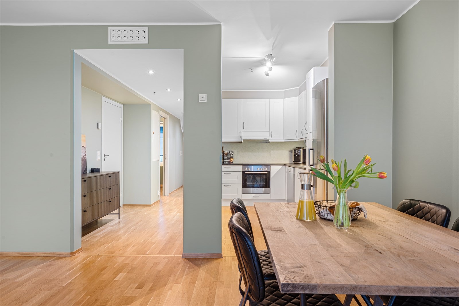 Den nesten åpne løsningen mellom kjøkken og stue skaper en naturlig og sosial sone, hvor de som lager mat enkelt kan være en del av det som skjer i stuen. Dette gir en fin flyt mellom rommene og gjør boligen ekstra trivelig i hverdagen Galleribilde