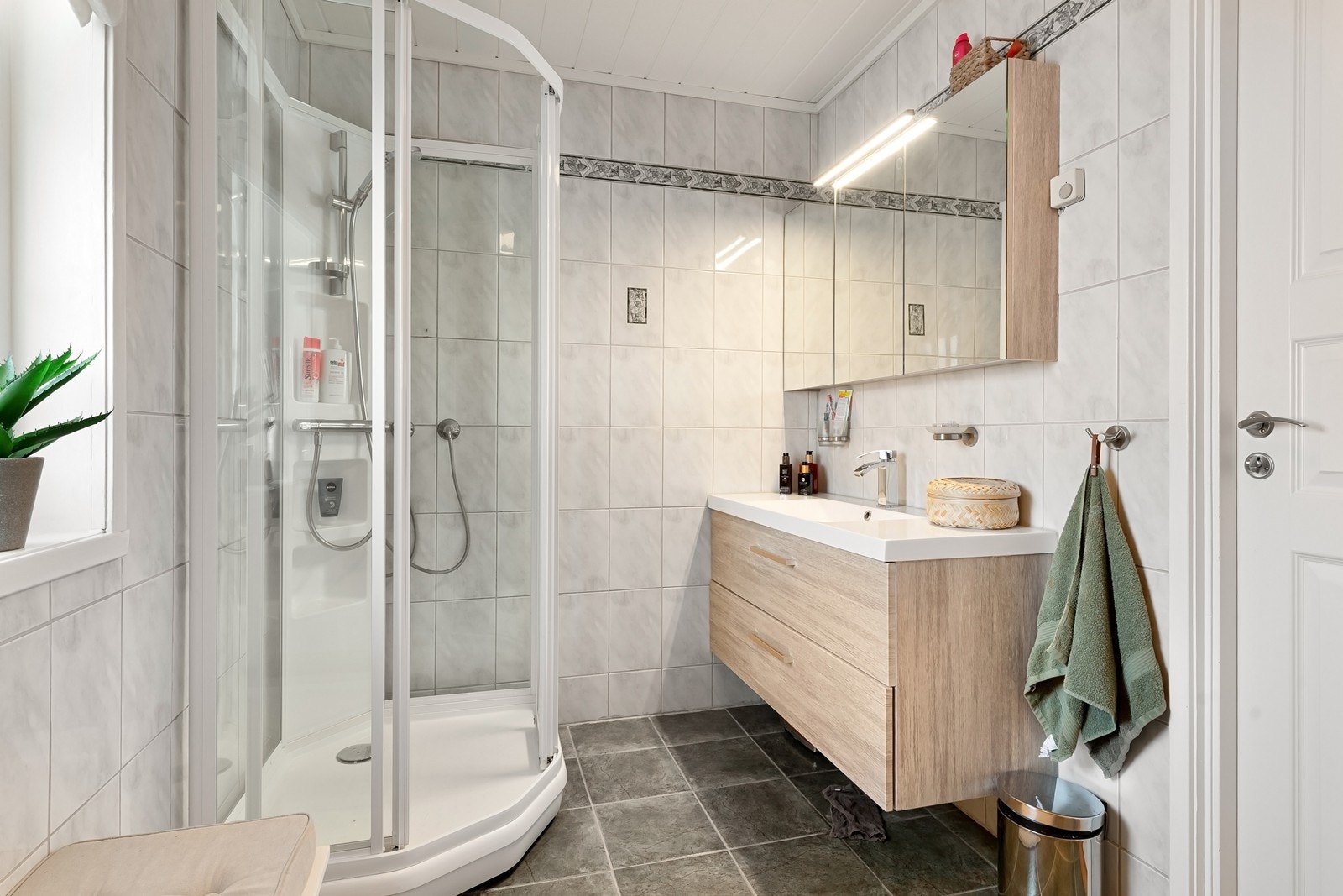 Badet er utstyrt med dusjkabinett og en stilren servantinnredning med skuffer. Galleribilde