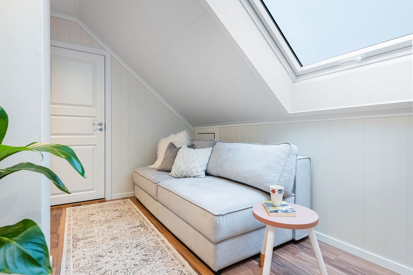 Koselig hjørne av loftstuen med takvindu som gir naturlig lysinnslipp. Praktisk lagrinsplass i knevegg bak døren ved sofaen, ideelt for oppbevaring av julepynt, kofferter og lignende. Galleribilde