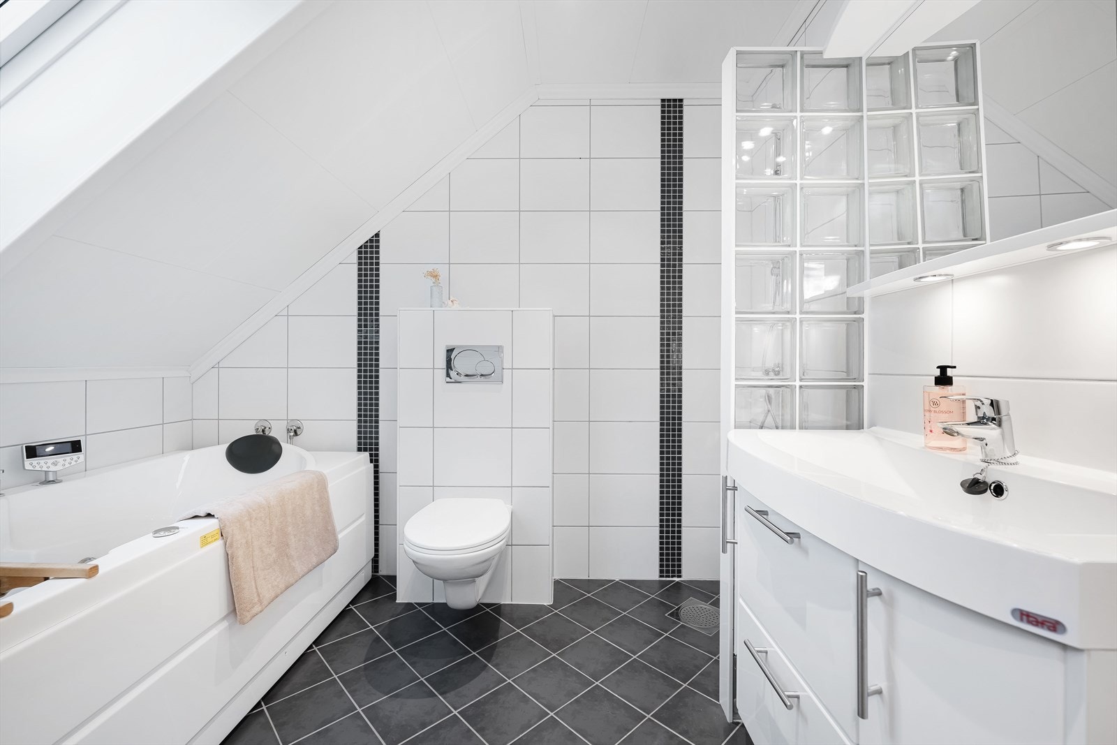 Rommet innehar servant med vegghengt toalett, dusjhjørne, badekar samt servant med nedfelt vask og speil med belysning over. Galleribilde