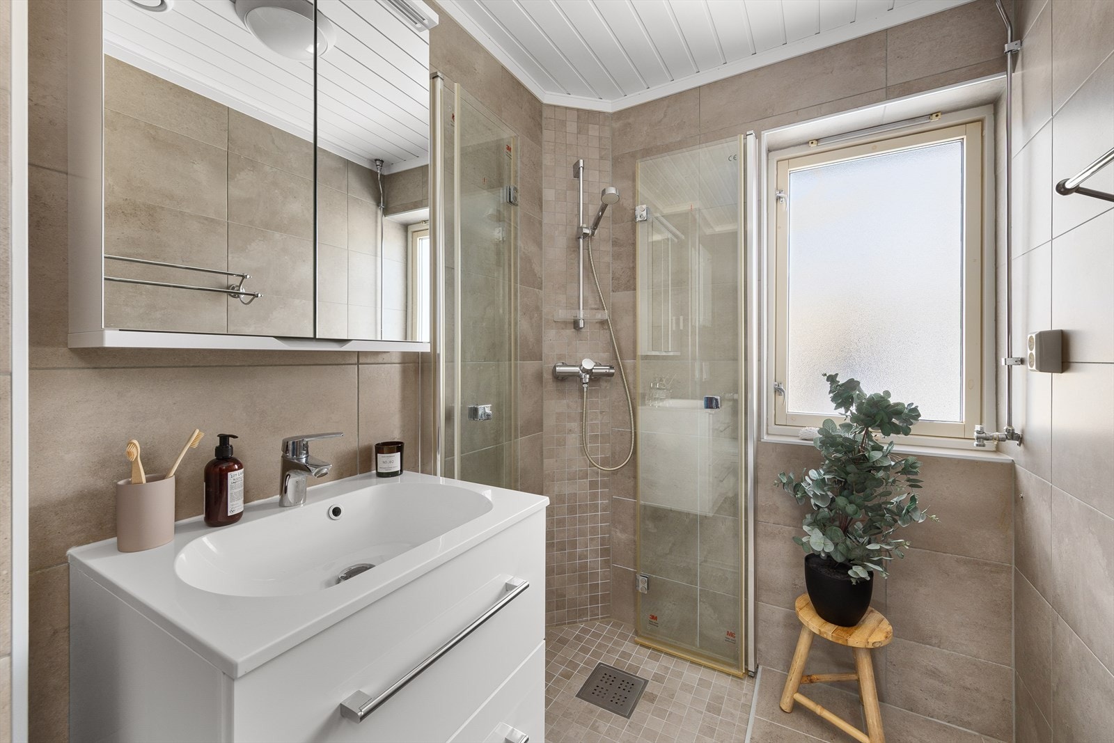 Innredningen inkluderer servant, veggmontert toalett, dusjhjørne og opplegg for vaskemaskin. Galleribilde