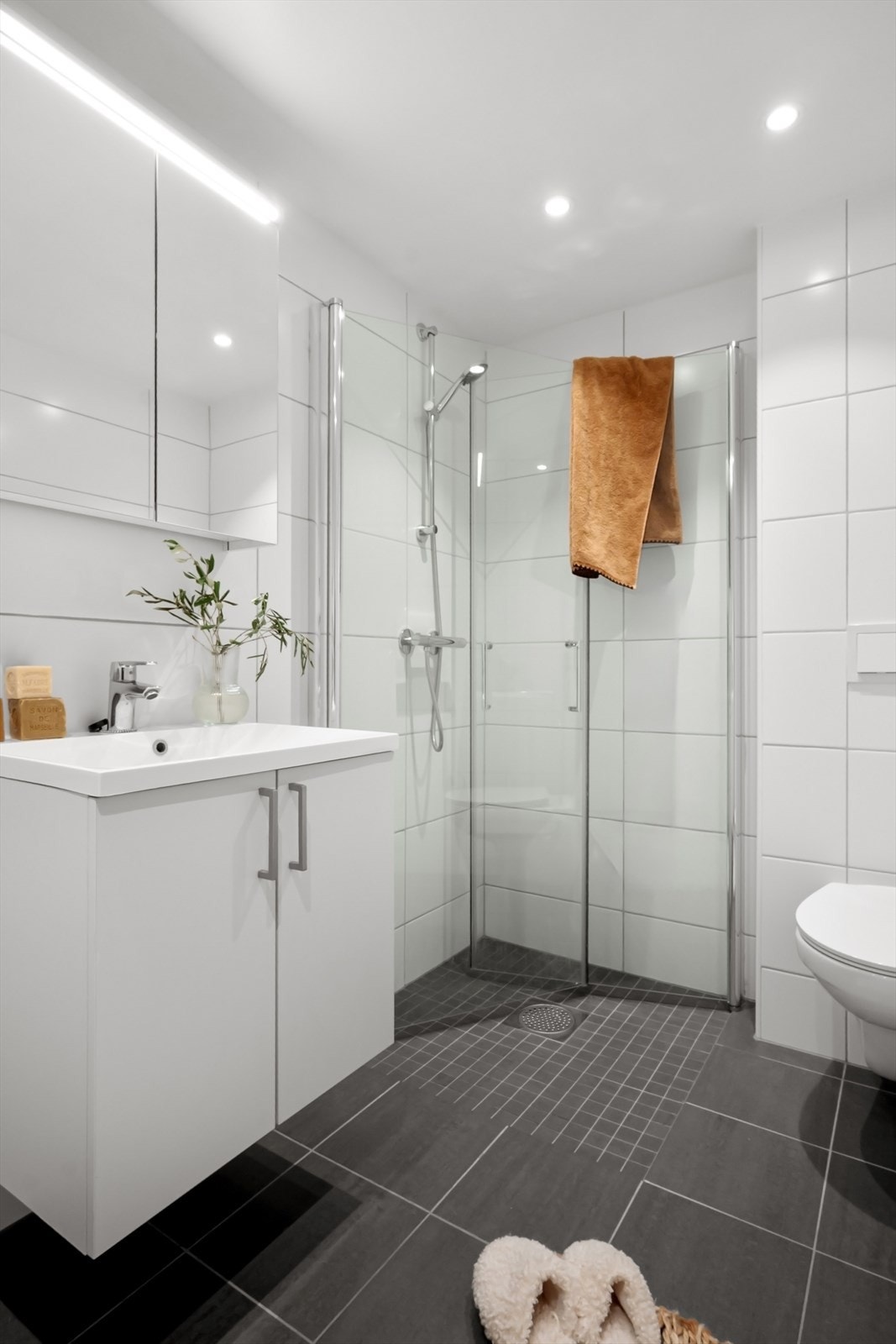 Baderomsinnredningen består av vegghengt klosett, servant med innredning, speilskap m/ lys og dusjhjørne med svingbare glassdører. Galleribilde