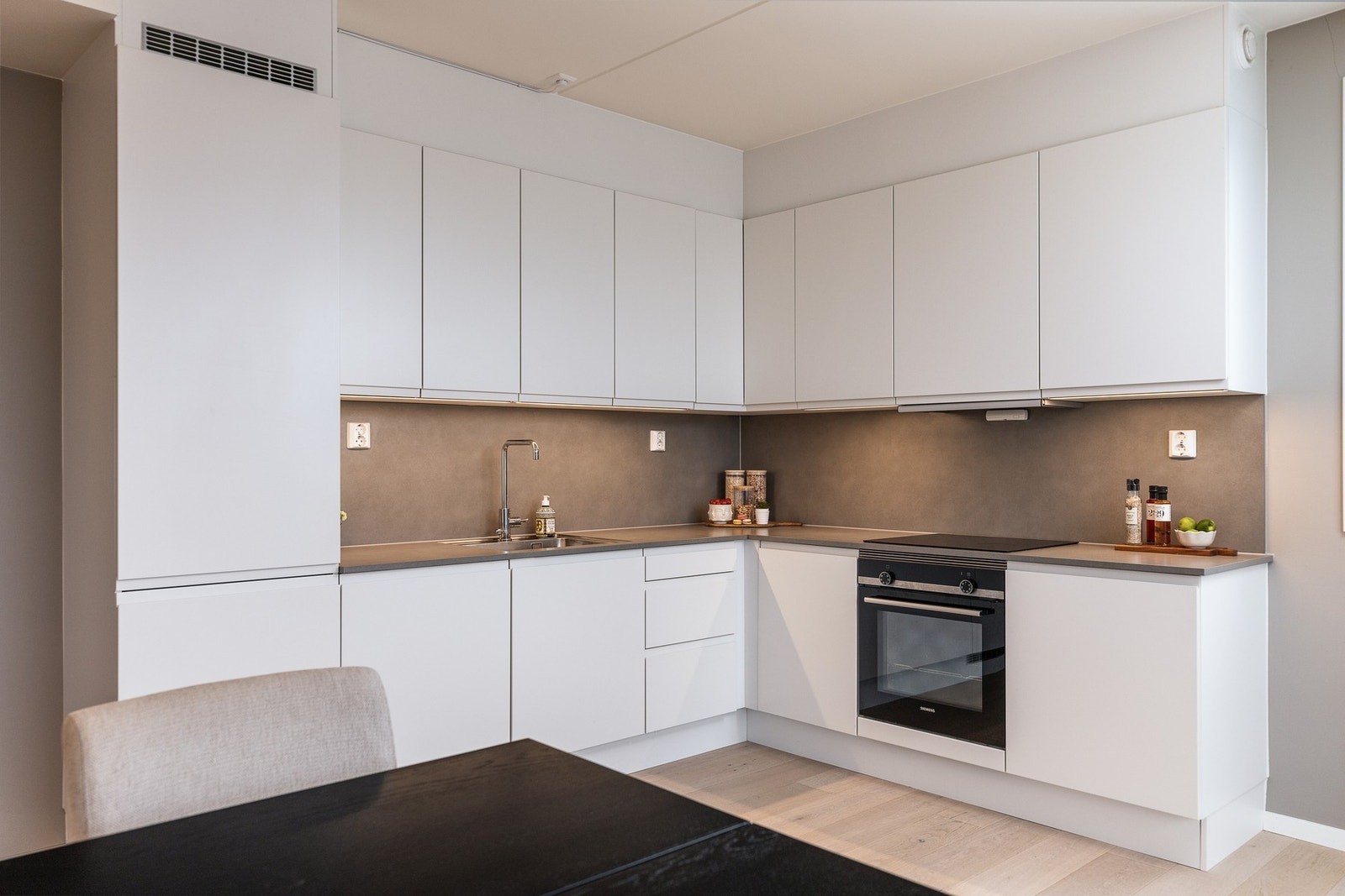 Kjøkkeninnredningen fra HTH har glatte, lyse fronter og platekledning på veggen over benkeskapene. Galleribilde