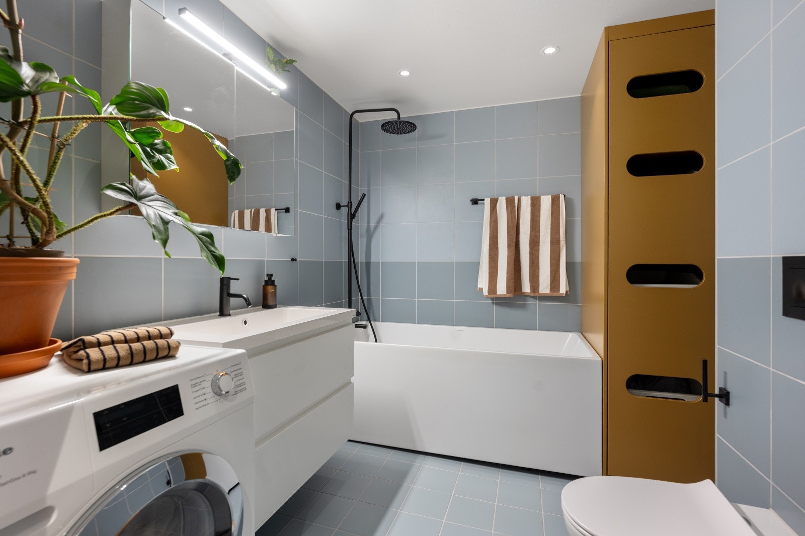 Moderne og lekkert baderom fra 2020 med vegghengt toalett, badekar, servantinnredning og opplegg for vaskemaskin. Galleribilde