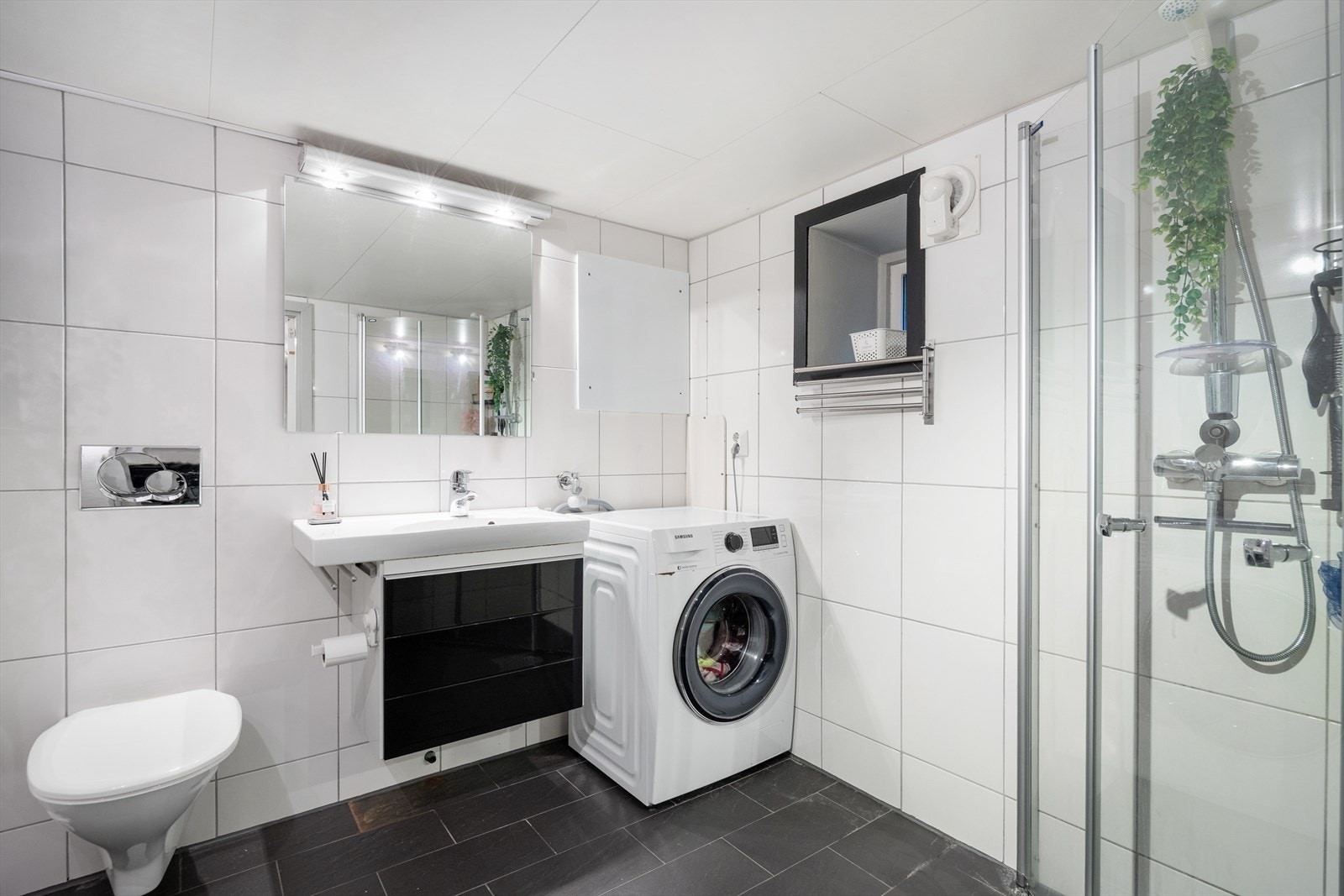 Keramiske fliser på gulv/vegger foruten en vegg med malt mur. Innredet med vegghengt toalett, dusj med glass foldedører, servant med møblement, speil og belysning. Røropplegg for vaskemaskin og sentral/skap for rør i rør system. Galleribilde