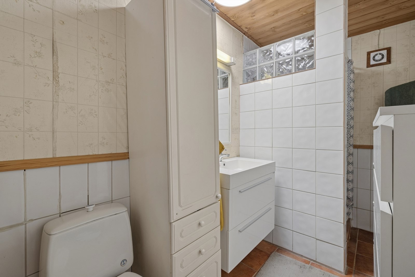 Baderom er flislagt med høyskap, frittstående toalett, servant med underskap og dusj på vegg. Galleribilde