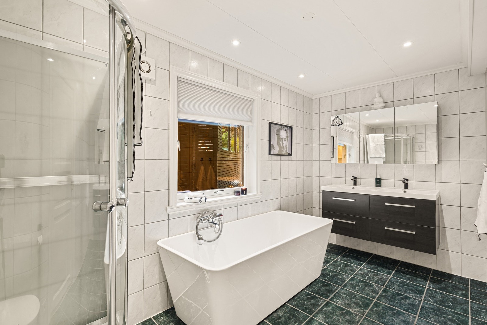 Badet inneholder stilrent vegghengt toalett, dobbel helstøpt servant, skuffer under servant med slette fronter, dusjkabinett og badekar. Galleribilde