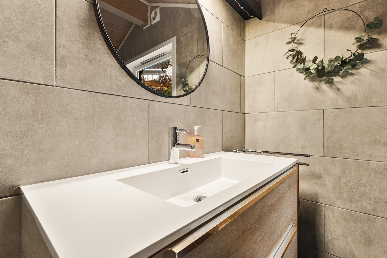 Badet inneholder vegghengt toalett, helstøpt servant, skuffer under servant med slette fronter og dusjdører i klart glass. Galleribilde