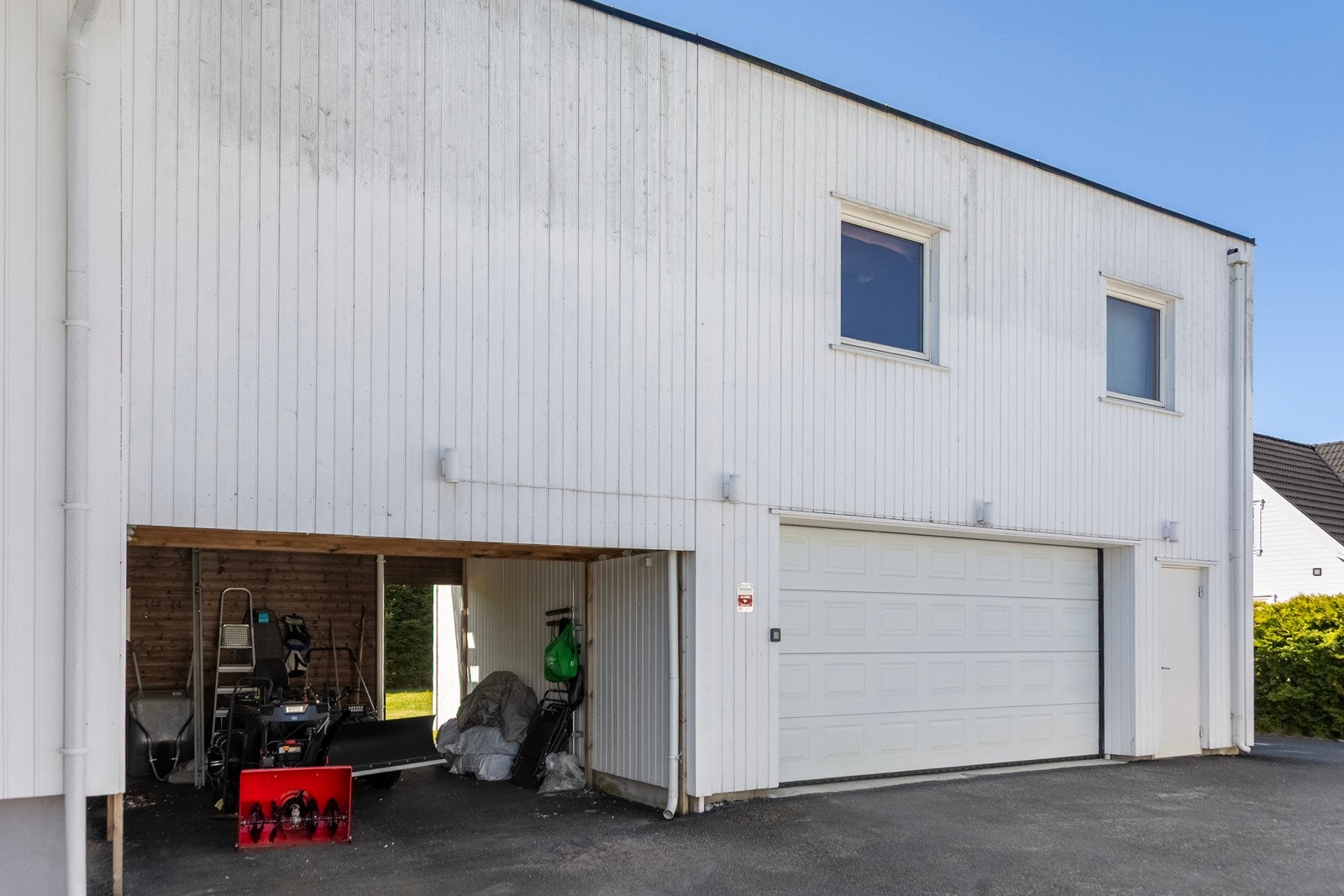 Stor asfaltert gårdsplass med dobbel garasje og carport med lader for elbil. Galleribilde