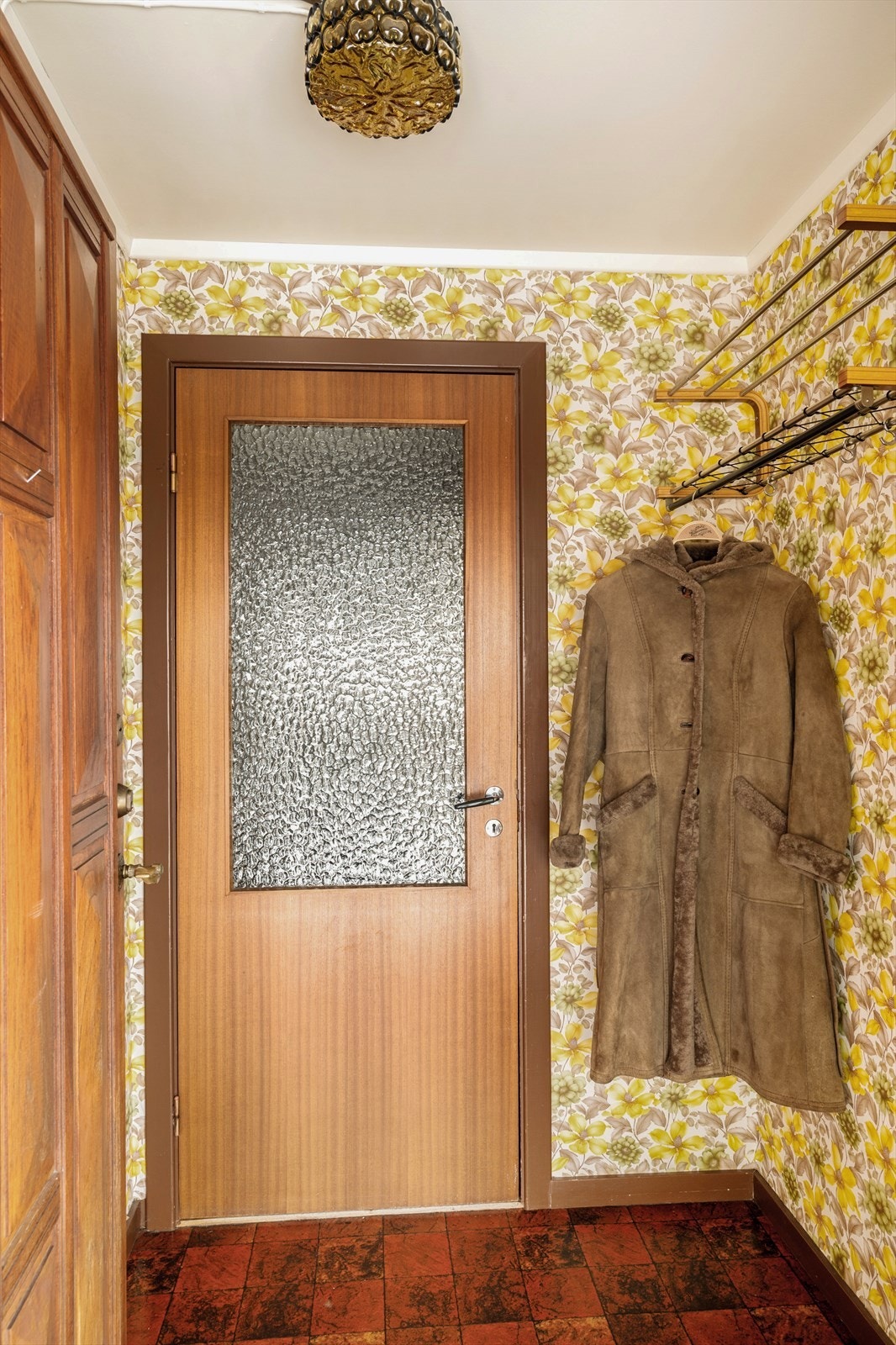 Det mørkerøde gulvbelegget, med sitt klassiske flisemønster, setter tonen idet du trer inn - lunt, karakterfullt og akkurat passe nostalgisk. Her møter du en solid teakdør som ønsker deg velkommen med den tyngden og varmen bare ekte treverk kan gi. Galleribilde