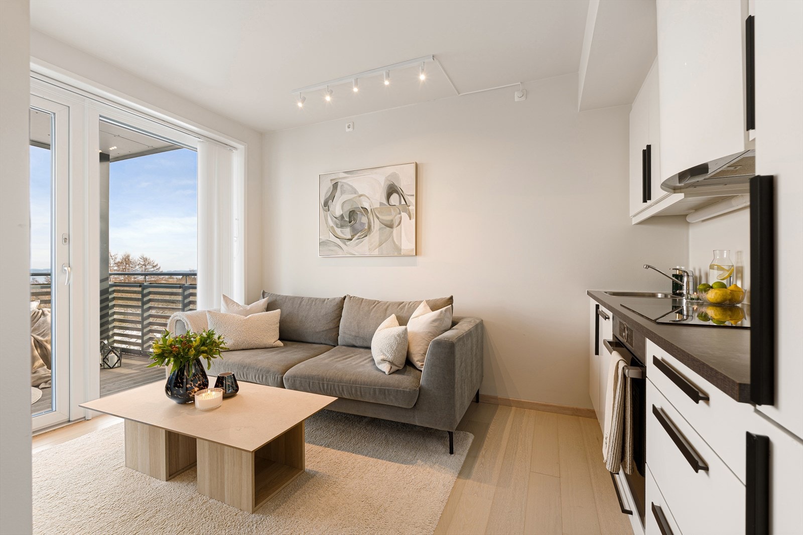 Boligens samlingspunkt inkluderer stue og kjøkken i en åpen løsning på 14 m². Allrommet får inn godt med naturlig dagslys fra de store vindusflatene som strekker seg helt fra gulvet og opp mot tak, noe som er med på å gjøre boligen lys og trivelig. Galleribilde