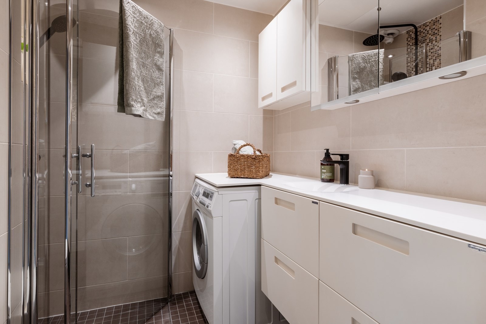 Flislagt bad/vaskerom innredet med servantskap med nedfelt servant (det opplyses om en liten sprekk i vasken), veggskap med speildører og belysning over. Galleribilde