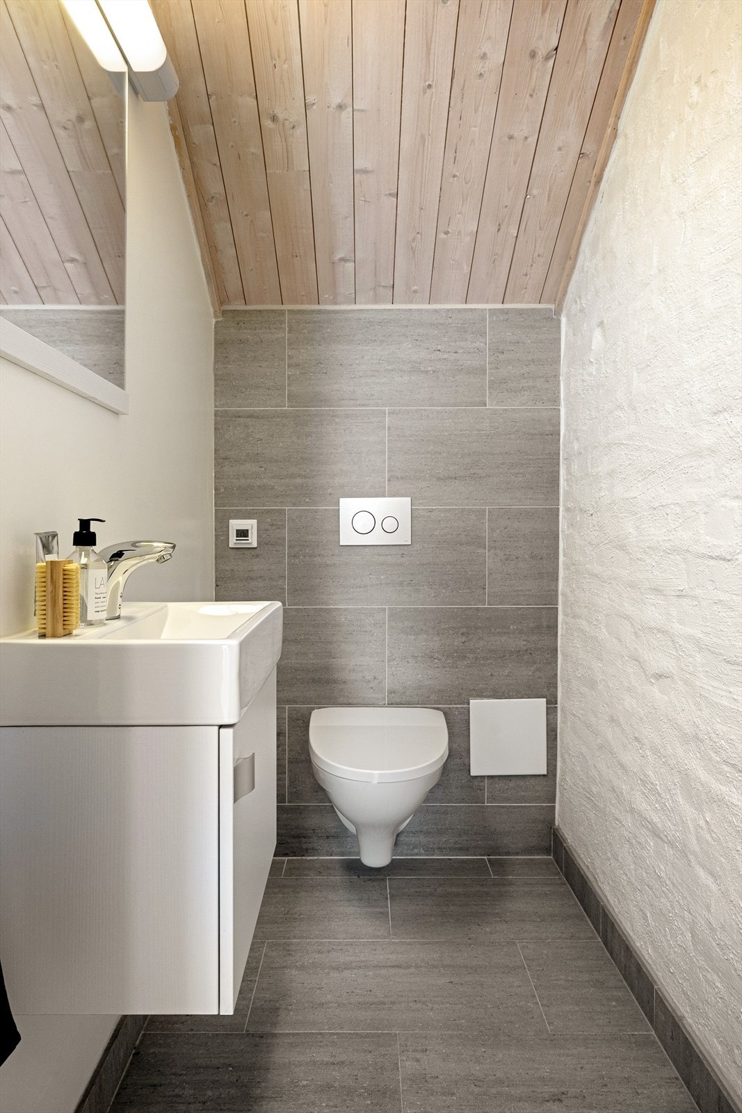 Vegg-i-vegg med badet er et funksjonelt toalettrom med toalett og servant, fliser på gulv og varmekabler. Galleribilde